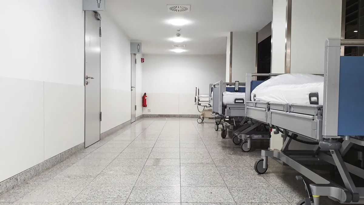 Krankenhauskorridor mit an der Wand neben den Stationstüren aufgereihten Patientenbetten