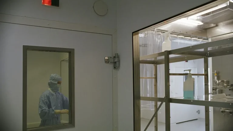Gowned operator visible through the window of a cleanroom airlock door with interlock indicator