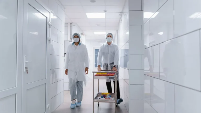 Gowned staff moving a sample cart through a white cleanroom corridor door