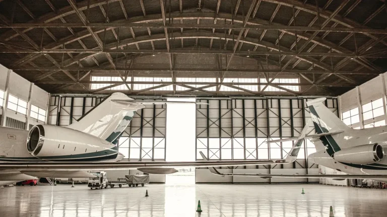 Wide hangar interior with the full-height door wall open behind two parked private jets