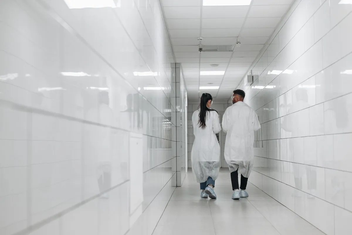 Staff in lab coats walking a bright tiled controlled facility corridor