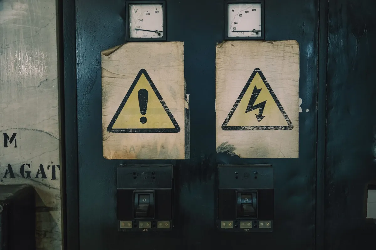 Yellow triangular hazard warning labels posted on a dark blue industrial electrical panel