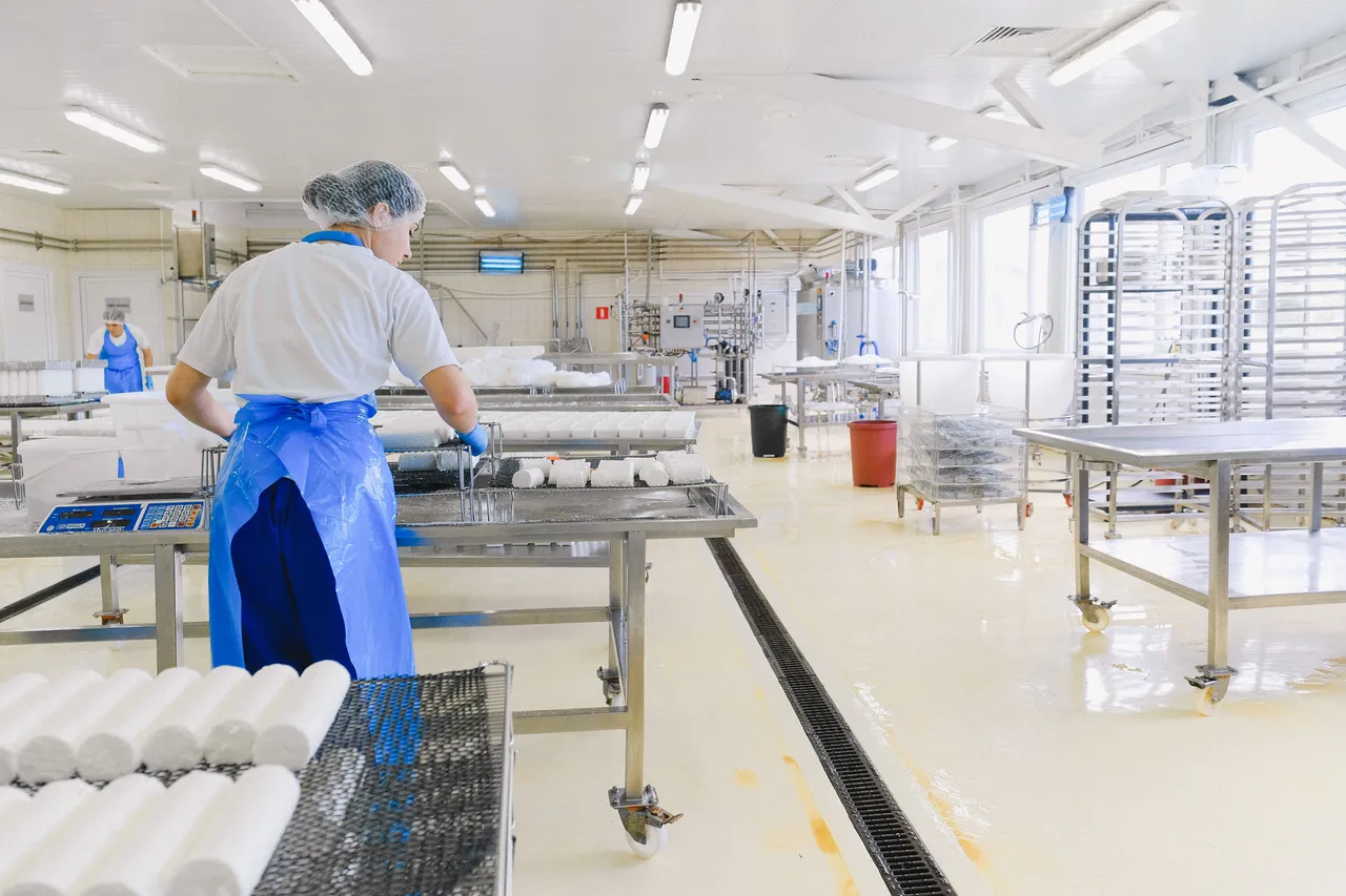 Mitarbeiter in einer Lebensmittelproduktionsanlage in Schutzausrüstung, der Geräte in der Nähe eines Edelstahl-Türbereichs reinigt