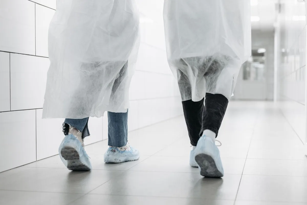 Staff fitting shoe covers before entering a controlled cleanroom corridor