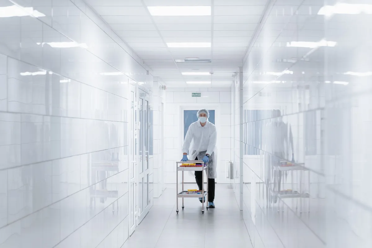 Technician moving a material cart through white cleanroom double doors