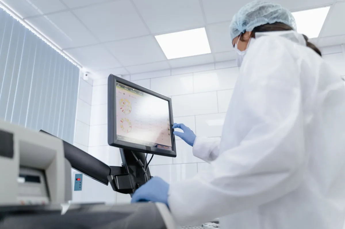 Femme en blouse de laboratoire utilisant un écran tactile dans un environnement de laboratoire moderne. (source: Pexels Commercial Free License)